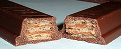 A Kit Kat broken in half showing a cross section of the bar - the chocolate outside and wafers within.