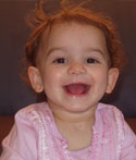 A baby wearing a pink top gives a big smile to the camera