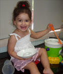 A toddler with bare feet smiles for the camera as she plays with a toy