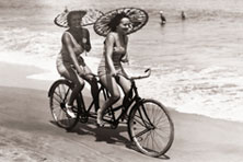 Two men on a tandem bike wearing trousers with the legs tucked into their socks