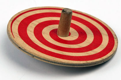 An old flat wooden spinning top with a red spiral painted around it and a small dowel in the middle