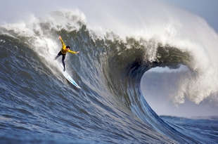 surf board rider riding down the face of a huge wave