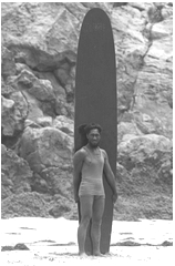 Surfer and Olympic swimmer Duke Kahanamoku standing on beach with surfboard in Los Angeles, CA.