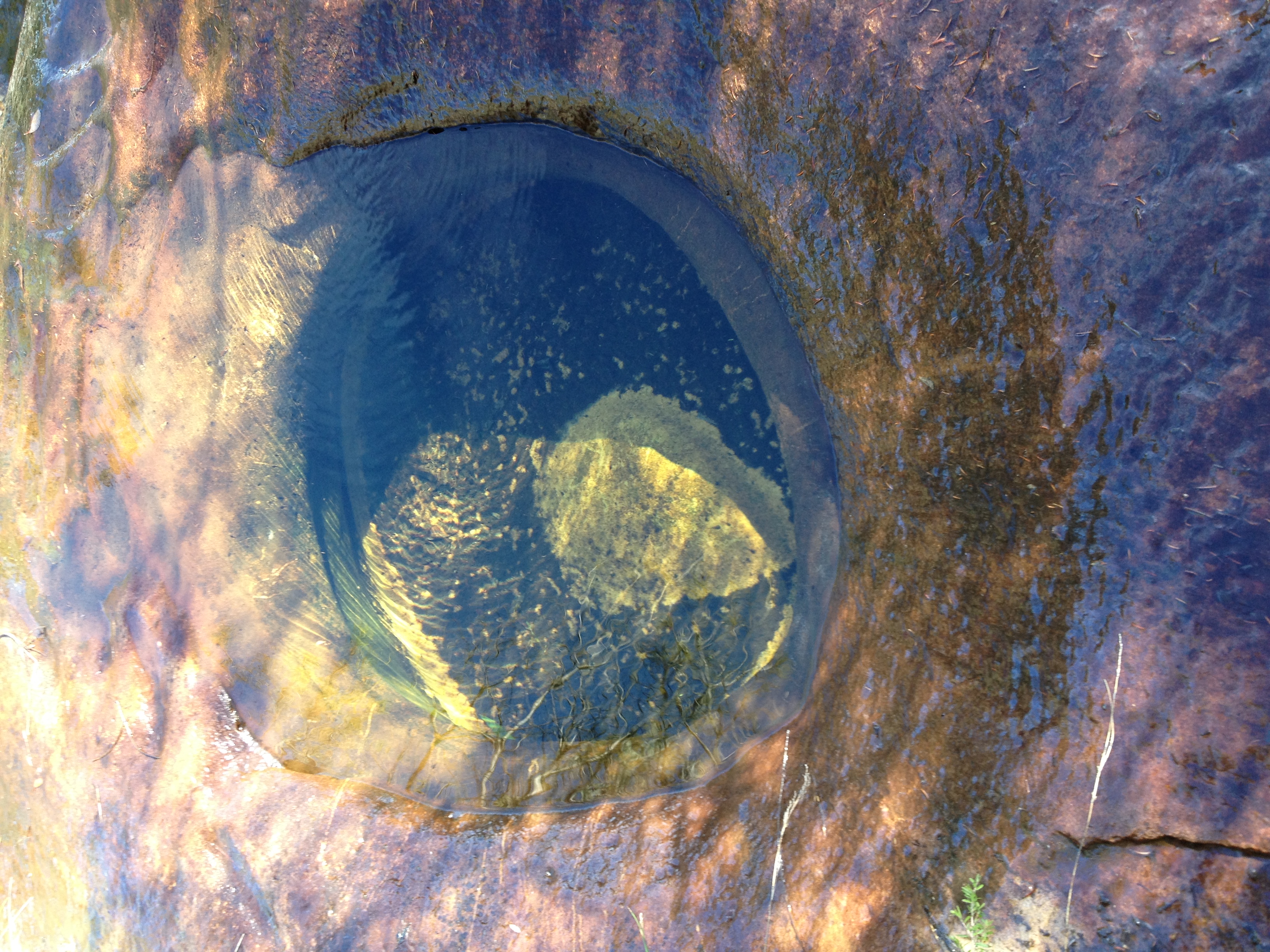 Top down view of a deeper pond within a wider shallow creek running over a rocky area. The water is very clear and clean.