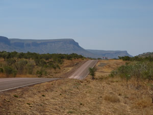 An empty road disappears over a low hill with rugged escarpment in the background An empty road disappears over a low hill with rugged escarpment in the background