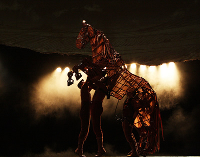 Two men lift the front of a life-size puppet horse.