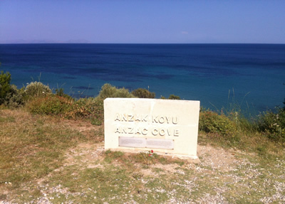 A plaque ANZAK KOYU/ANZAC COVE— on a grassy cliff top overlooking water. A plaque ANZAK KOYU/ANZAC COVE— on a grassy cliff top overlooking water.