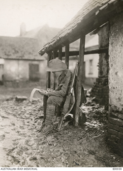 A soldier sits one the edge of a verandah, surrounded by muddy ground, writing on note paper A soldier sits one the edge of a verandah, surrounded by muddy ground, writing on note paper