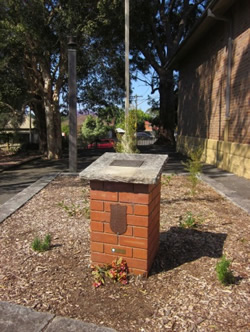 A small bick pillar with a plaque on the top and side in a garden.