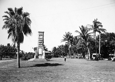 A lawn with a tall, thin monument and palm trees A lawn with a tall, thin monument and palm trees