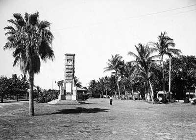 A lawn with a tall, thin monument and palm trees