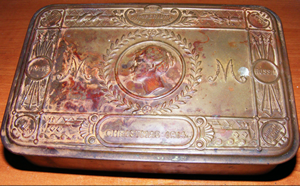 A metal tin with carved border and centre cameo; the letters M are on either side. A metal tin with carved border and centre cameo; the letters M are on either side.
