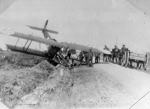A plane lies nose down in a ditch as soldiers wait nearby and others on horseback and driving a horse and cart pass by. A plane lies nose down in a ditch as soldiers wait nearby and others on horseback and driving a horse and cart pass by.