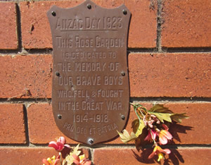 Plaque on a brick wall with some flowers. The plaque reads: 'Anzac Day 1923—This rose garden is dedicated to the memory of our brave boys who feel and fought in The Great War 1914-1915 – Pro deo et patria' Plaque on a brick wall with some flowers. The plaque reads: 'Anzac Day 1923—This rose garden is dedicated to the memory of our brave boys who feel and fought in The Great War 1914-1915 – Pro deo et patria'